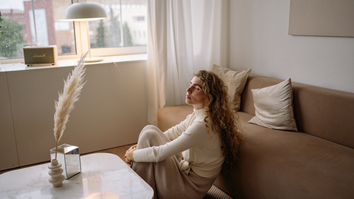 A woman sitting on a sofa in a calm, minimalist living room setting.